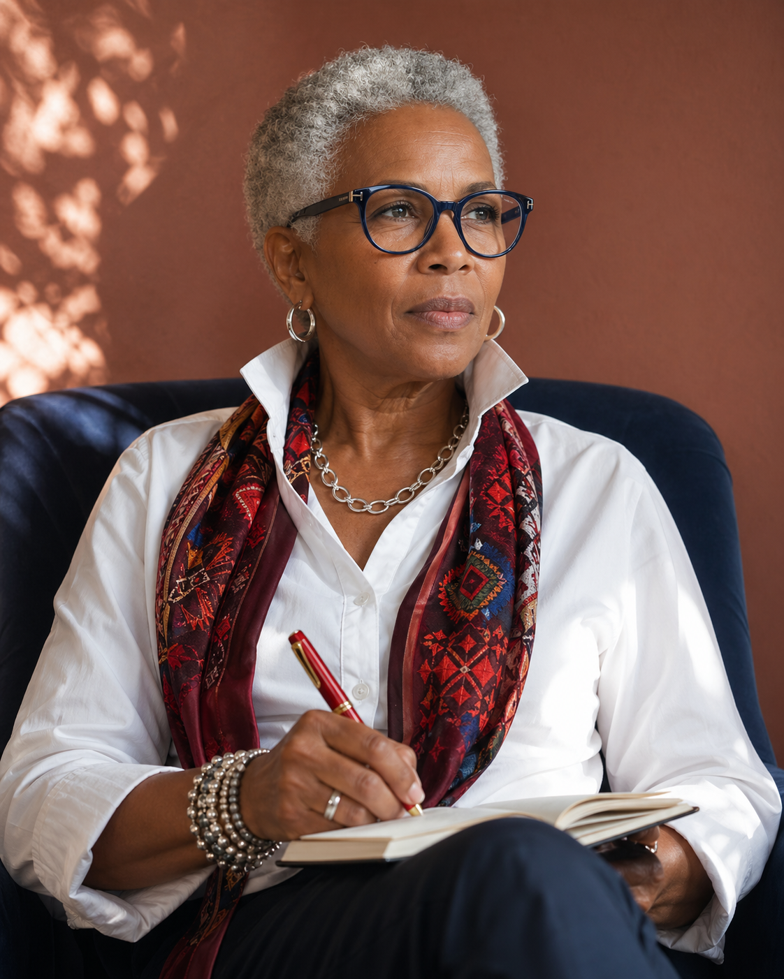 Woman in glasses, smiling, wearing a white shirt and patterned scarf.
